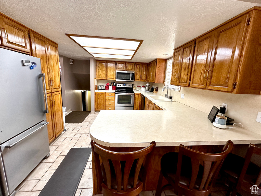 Kitchen featuring appliances with stainless steel finishes, brown cabinets, light countertops, a peninsula, and a textured ceiling