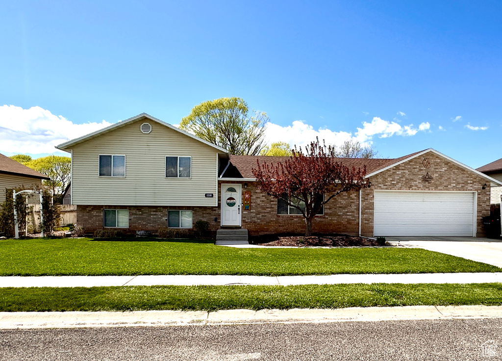 Split level home featuring a garage, brick siding, driveway, and a front yard