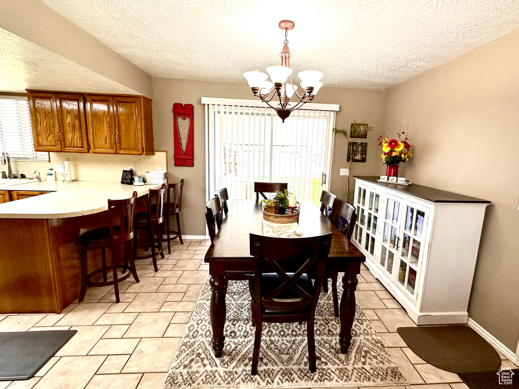 Dining space featuring healthy amount of natural light, a textured ceiling, a chandelier, and light tile patterned floors