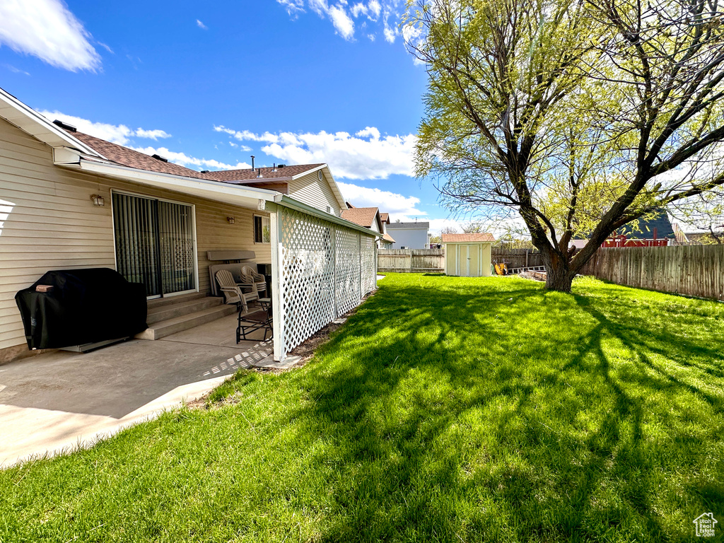 Fenced backyard featuring a storage unit and a patio area