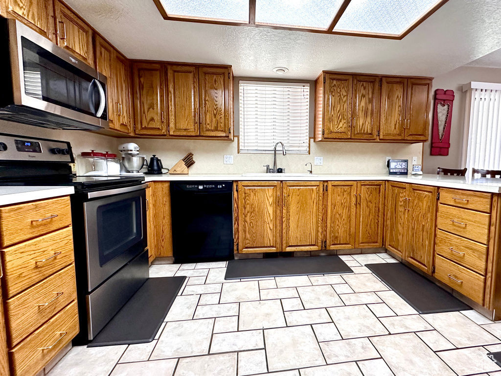 Kitchen with appliances with stainless steel finishes, light countertops, brown cabinetry, and a textured ceiling