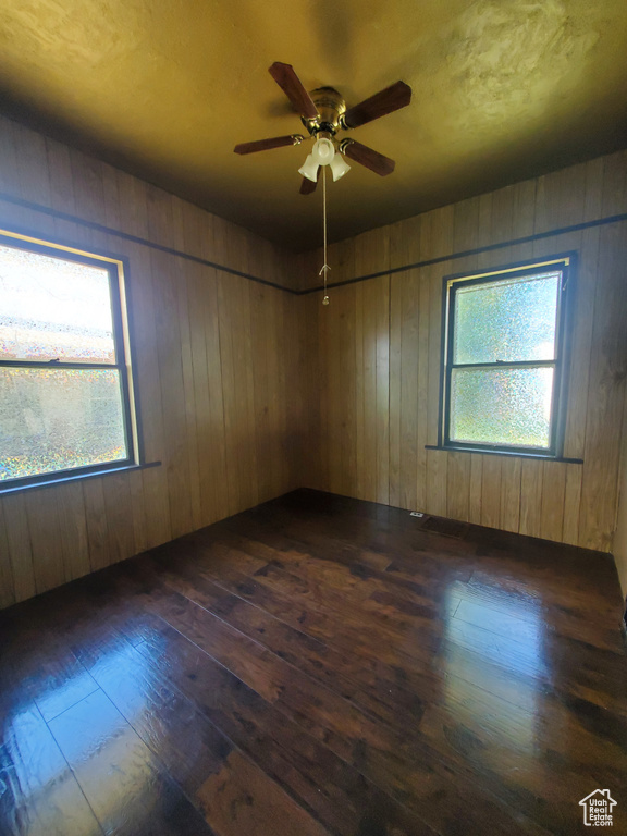 Spare room featuring dark wood-style flooring, healthy amount of natural light, ceiling fan, and wood walls