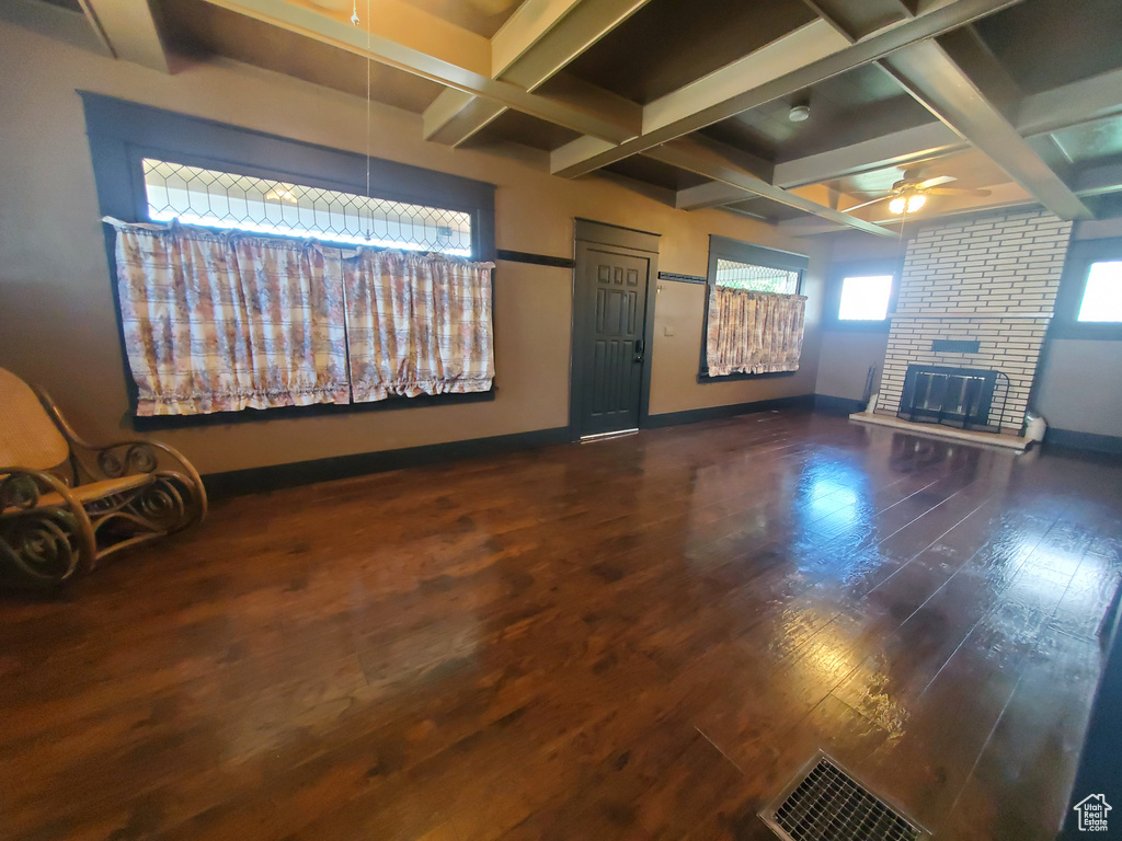 Unfurnished living room featuring coffered ceiling, a ceiling fan, a fireplace, wood finished floors, and beamed ceiling