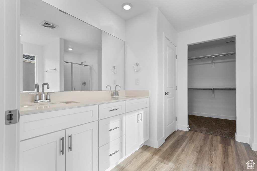 Full bathroom with a stall shower, double vanity, a spacious closet, and wood finished floors