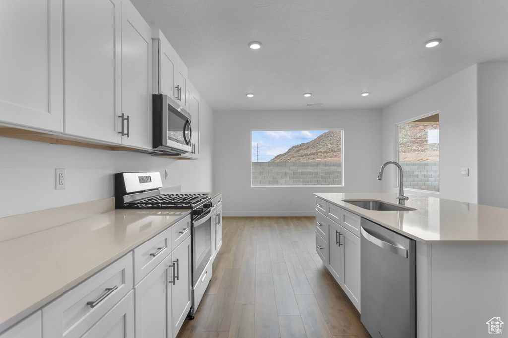 Kitchen featuring stainless steel appliances, wood finished floors, light countertops, recessed lighting, and white cabinets