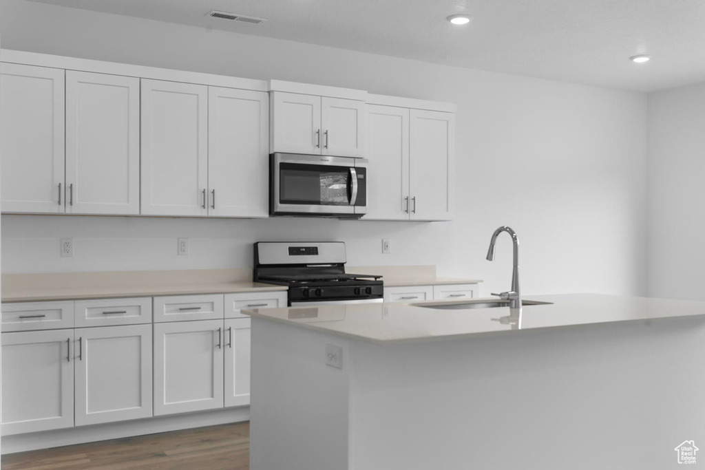 Kitchen with black gas stove, stainless steel microwave, light countertops, a center island with sink, and recessed lighting