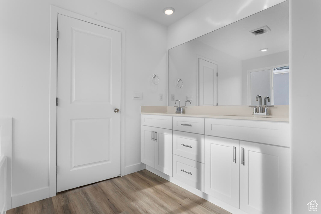 Bathroom featuring double vanity, wood finished floors, and recessed lighting