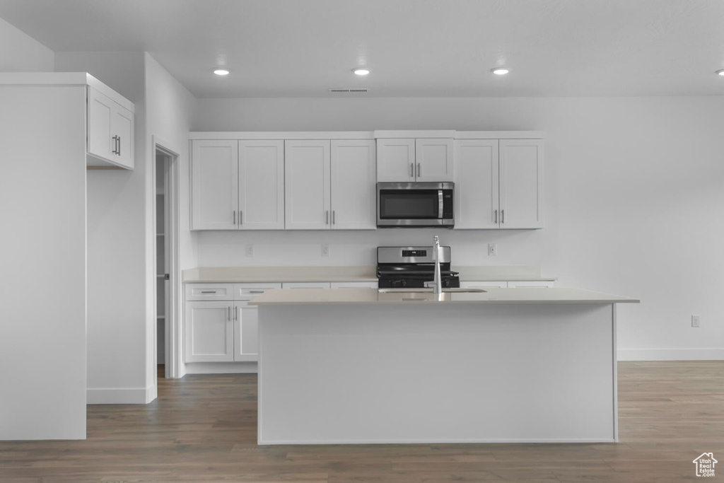 Kitchen featuring appliances with stainless steel finishes, wood finished floors, light countertops, a kitchen island with sink, and recessed lighting