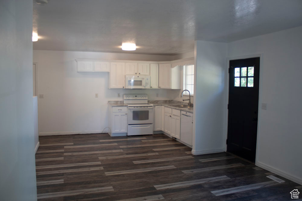 Kitchen with white appliances, white cabinetry, dark wood-style floors, and light countertops