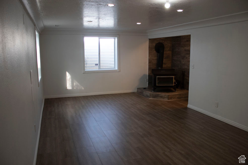 Unfurnished living room featuring a wood stove, ornamental molding, and wood finished floors