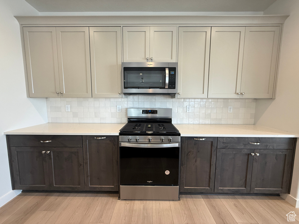 Kitchen with appliances with stainless steel finishes, light wood-style floors, light countertops, and backsplash