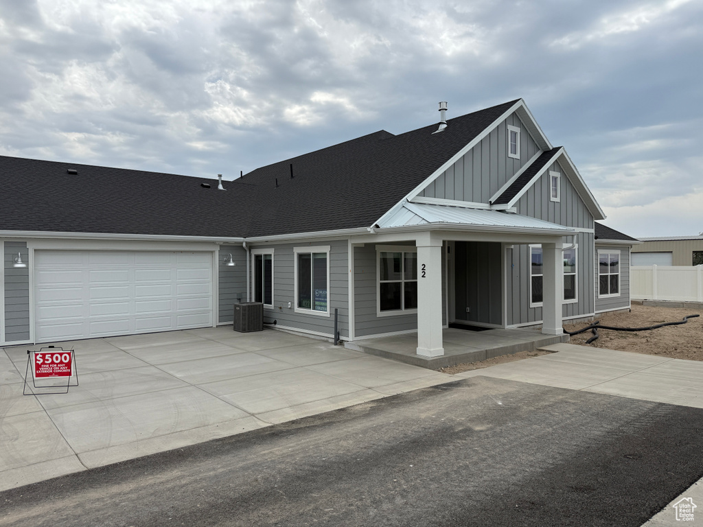 View of front of house with board and batten siding, a shingled roof, concrete driveway, a garage, and covered porch