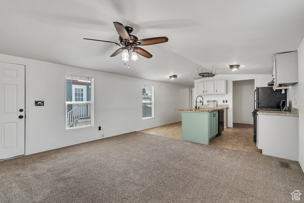 Kitchen with light carpet, a ceiling fan, open floor plan, refrigerator, and white cabinets