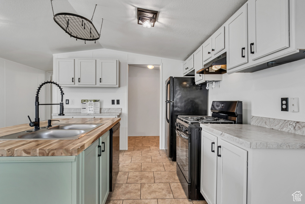 Kitchen featuring butcher block counters, black appliances, vaulted ceiling, under cabinet range hood, and white cabinets