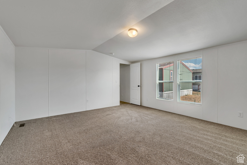 Carpeted spare room featuring lofted ceiling