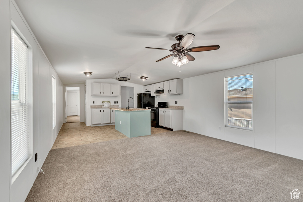 Kitchen with an island with sink, light colored carpet, black appliances, vaulted ceiling, and white cabinetry