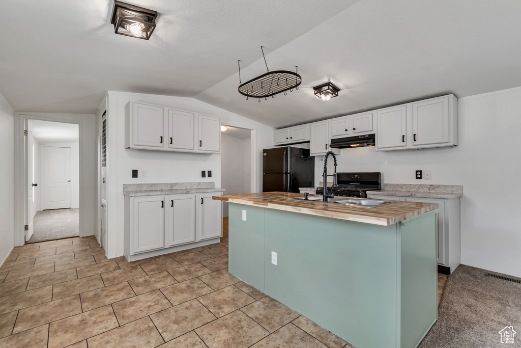 Kitchen with white cabinetry, black appliances, an island with sink, butcher block counters, and under cabinet range hood