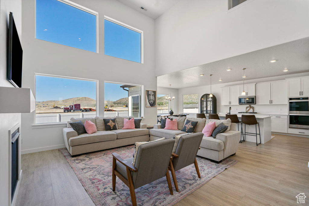 Living area featuring light wood-style flooring, a high ceiling, a chandelier, and recessed lighting