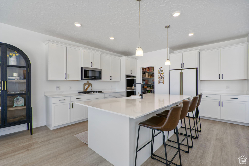 Kitchen with stainless steel appliances, light wood-style floors, a breakfast bar, light countertops, and white cabinets