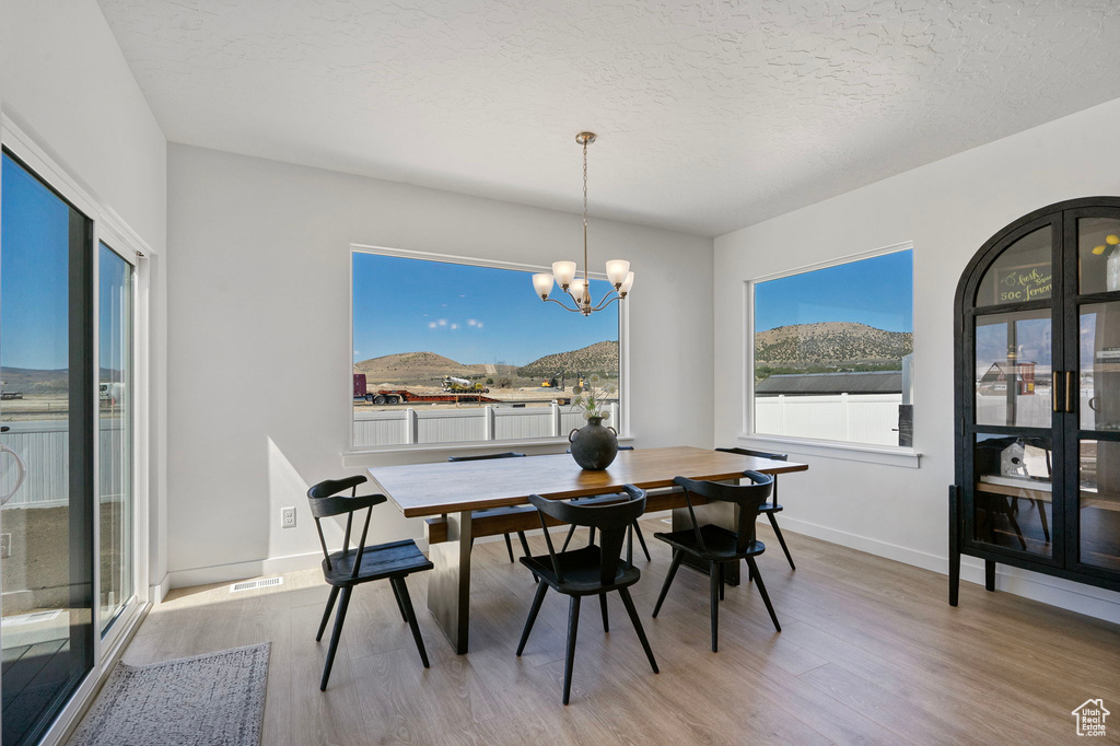 Dining area with light wood-type flooring, a chandelier, a textured ceiling, and a mountain view