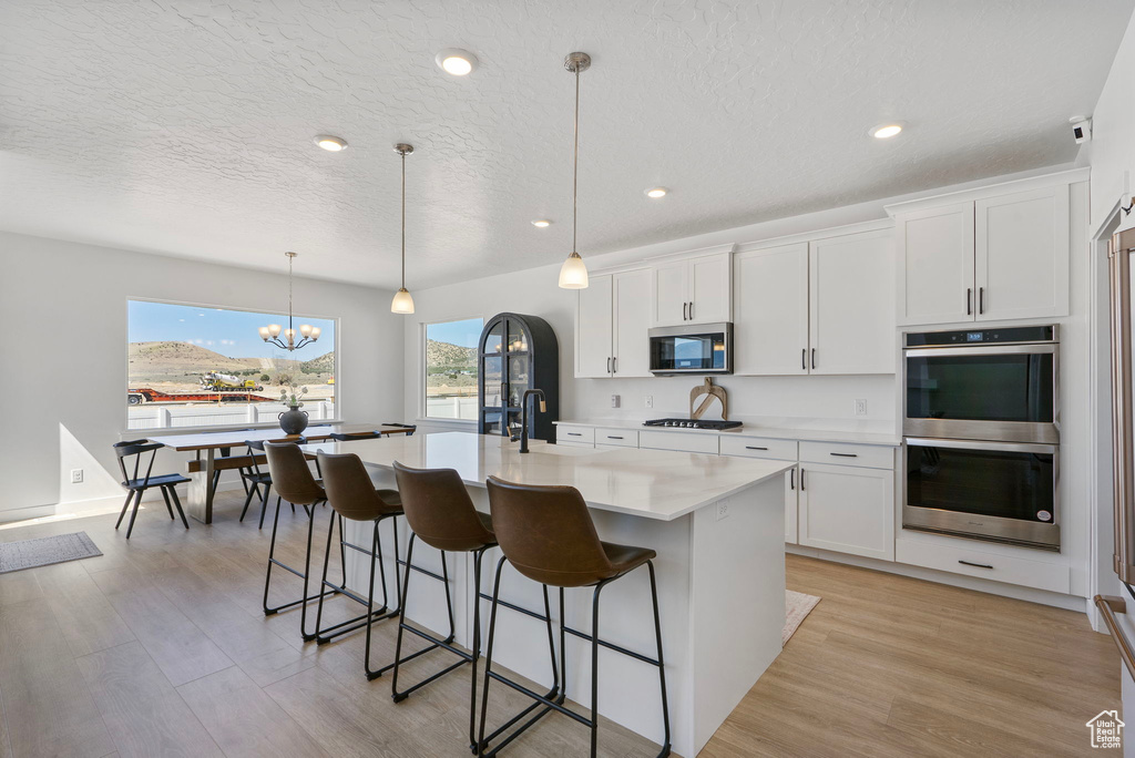 Kitchen featuring appliances with stainless steel finishes, a kitchen bar, a kitchen island with sink, light countertops, and a chandelier