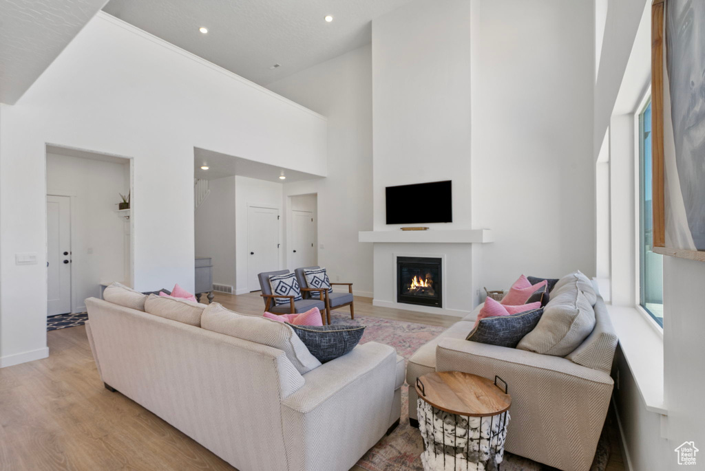 Living room with light wood finished floors, a lit fireplace, recessed lighting, and a towering ceiling