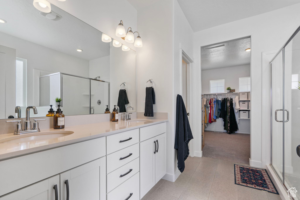 Full bath featuring a shower stall, double vanity, a spacious closet, tile patterned flooring, and recessed lighting