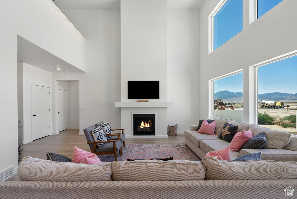 Living room with a high ceiling, a lit fireplace, and wood finished floors