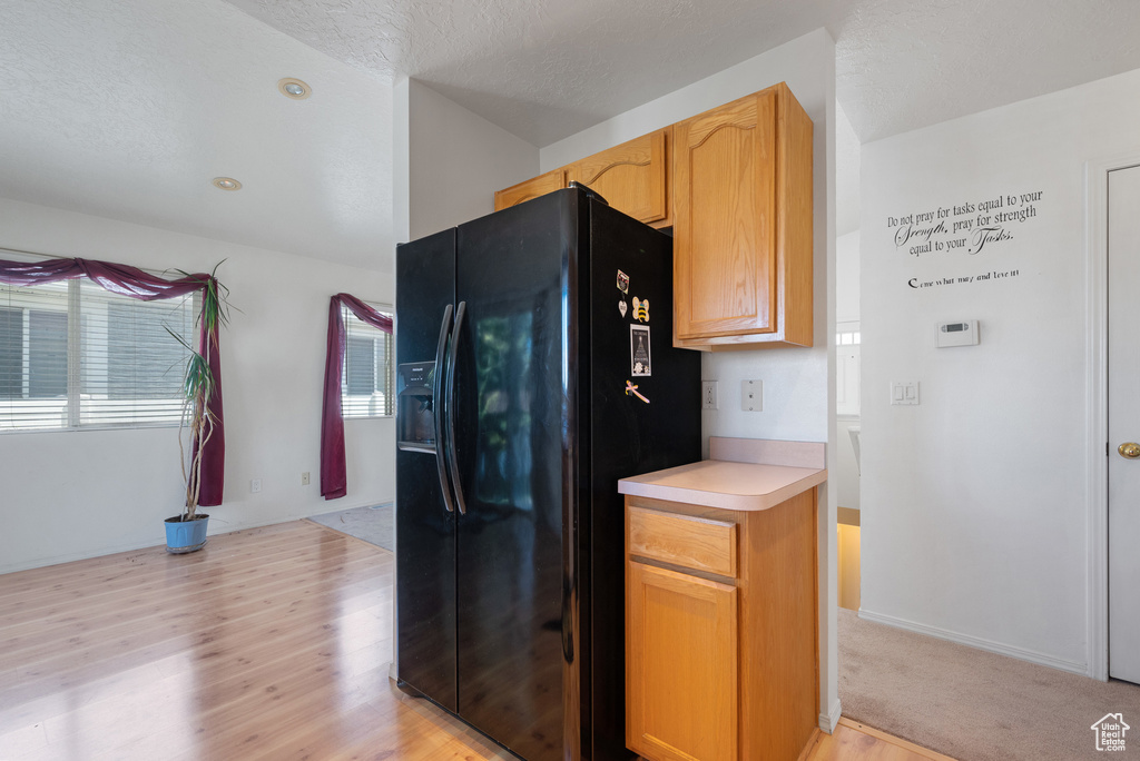 Kitchen with black fridge, light wood-style flooring, light countertops, and healthy amount of natural light
