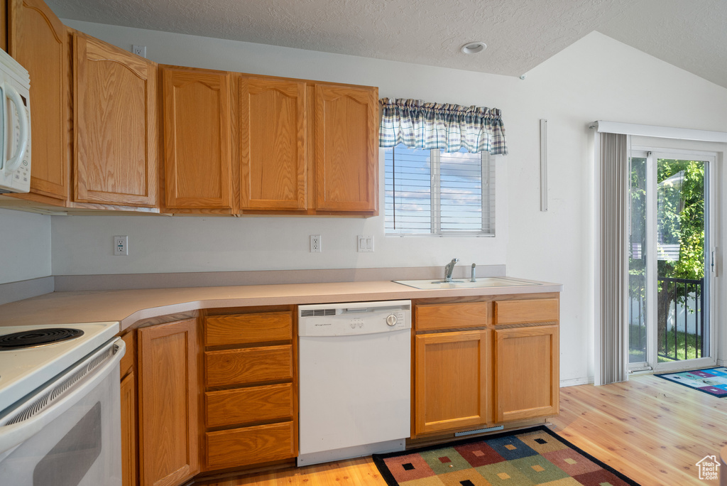 Kitchen featuring white appliances, light wood-style floors, light countertops, healthy amount of natural light, and a textured ceiling