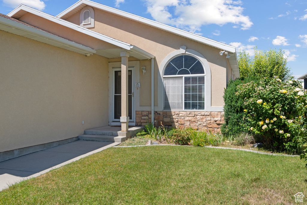 View of exterior entry featuring a lawn, stucco siding, and stone siding