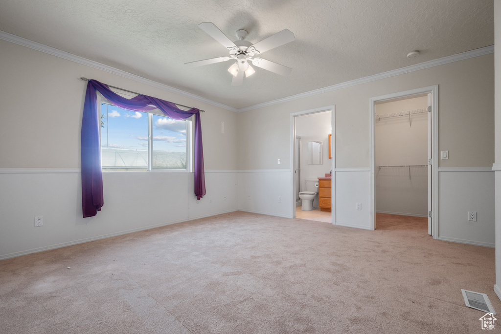 Unfurnished bedroom with a textured ceiling, a spacious closet, crown molding, carpet, and ensuite bathroom
