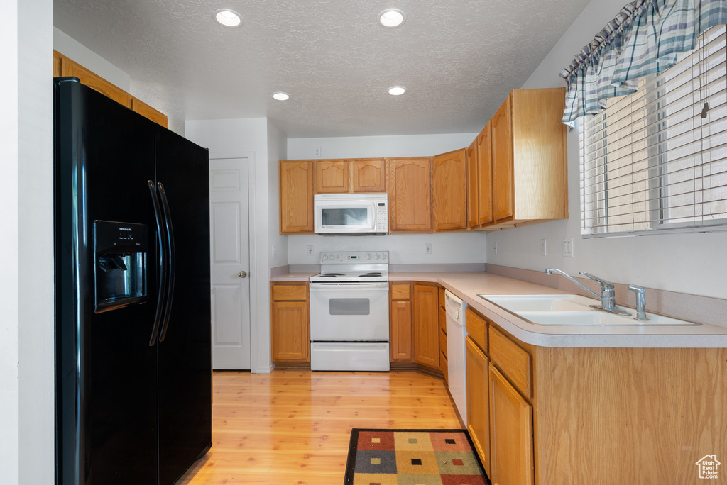 Kitchen with white appliances, light countertops, light wood-style flooring, a textured ceiling, and recessed lighting