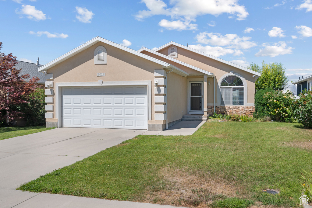 Ranch-style home featuring stucco siding, a front lawn, an attached garage, concrete driveway, and stone siding