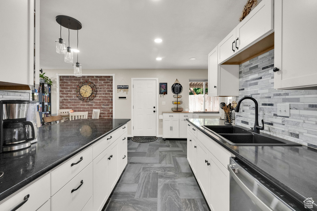 Kitchen with tasteful backsplash, stainless steel dishwasher, white cabinetry, hanging light fixtures, and dark stone counters
