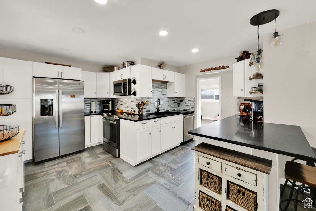 Kitchen featuring stainless steel appliances, decorative backsplash, dark countertops, white cabinets, and recessed lighting