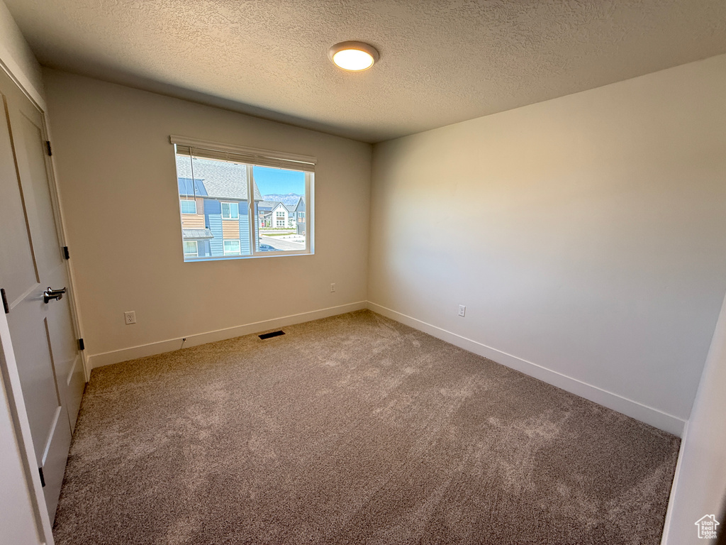 Carpeted empty room with a textured ceiling and baseboards