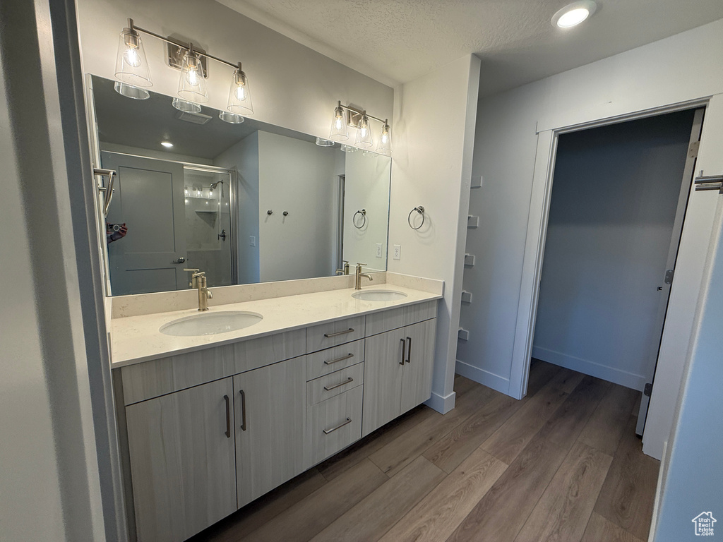 Bathroom featuring double vanity, wood finished floors, a stall shower, and a textured ceiling