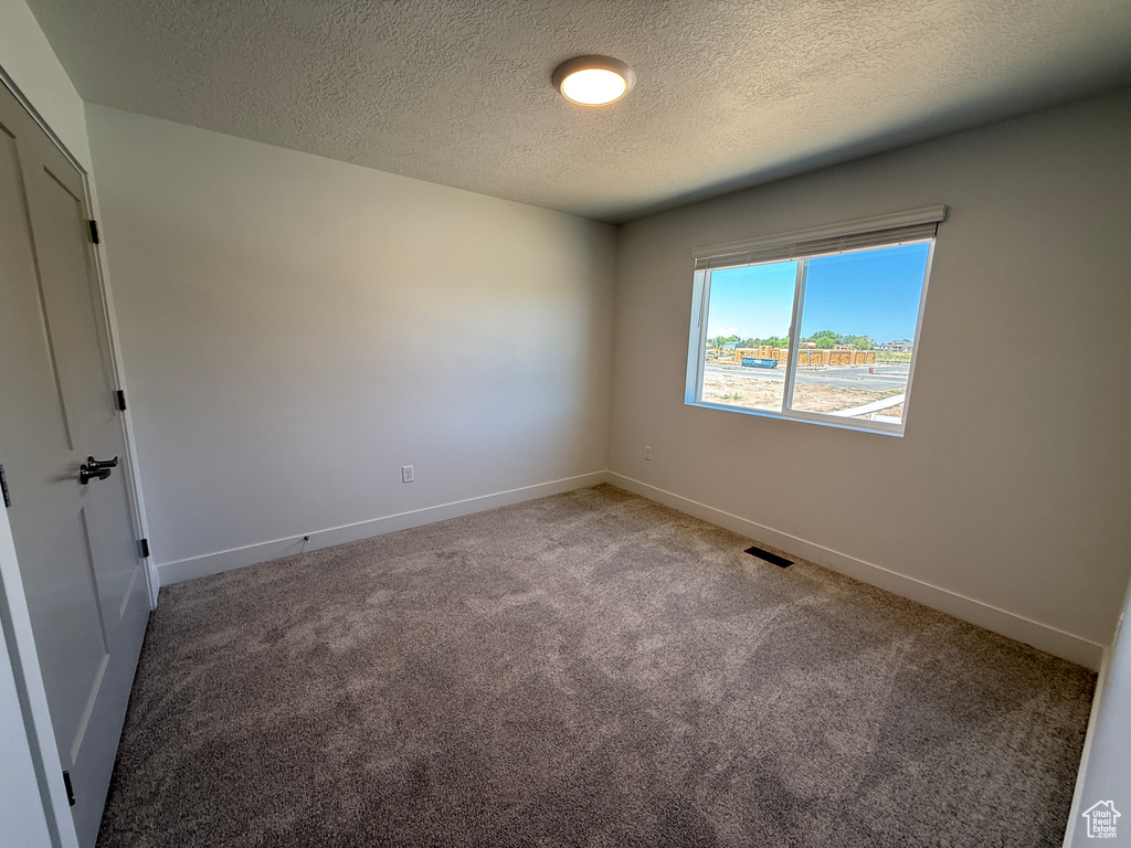 Empty room with light carpet and a textured ceiling