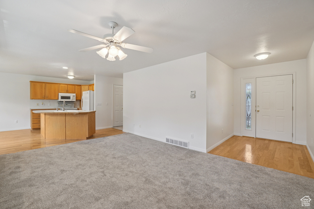 Kitchen featuring open floor plan, light colored carpet, light countertops, ceiling fan, and white appliances