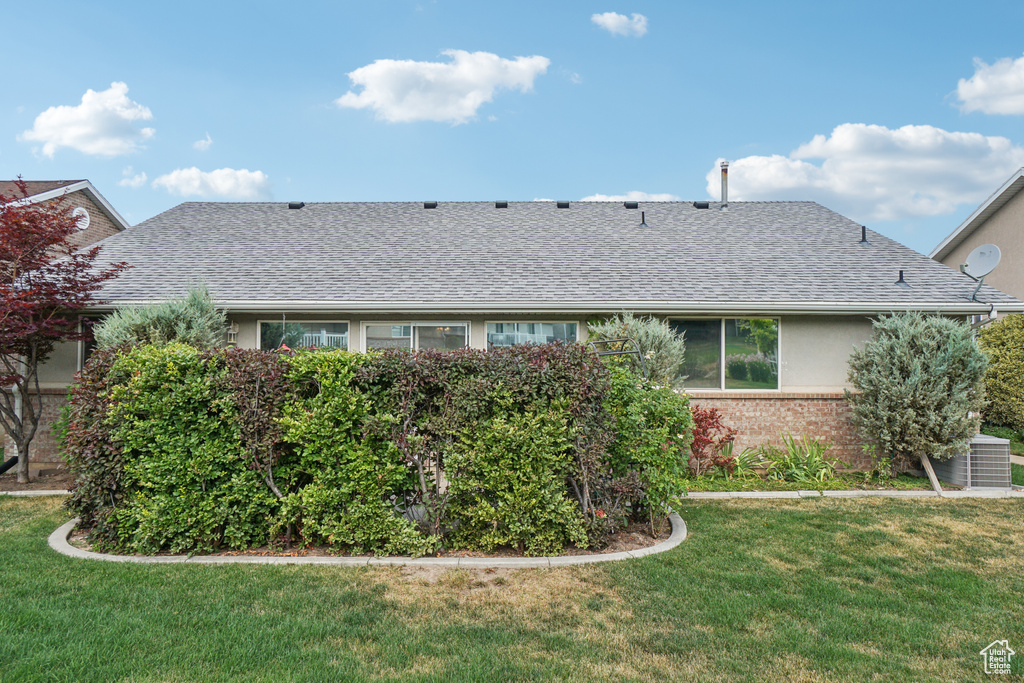 Back of property with a shingled roof, brick siding, and a yard
