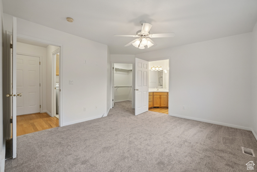 Unfurnished bedroom featuring light colored carpet, a walk in closet, connected bathroom, and a ceiling fan