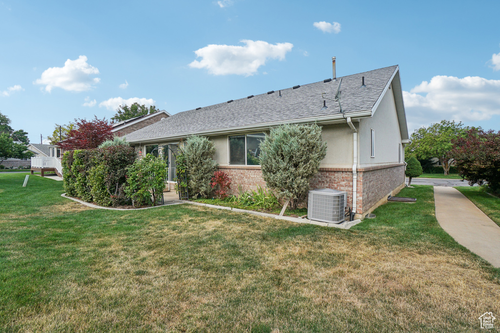 View of side of property with brick siding, stucco siding, a lawn, and a shingled roof