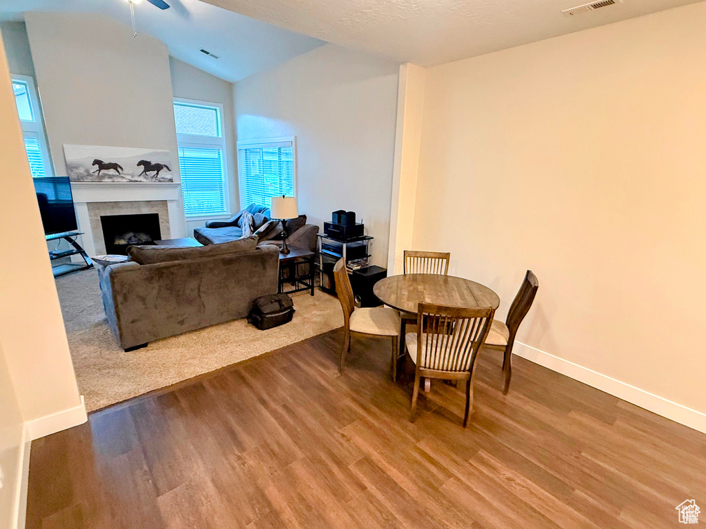 Dining room with wood finished floors, lofted ceiling, a fireplace, and a ceiling fan