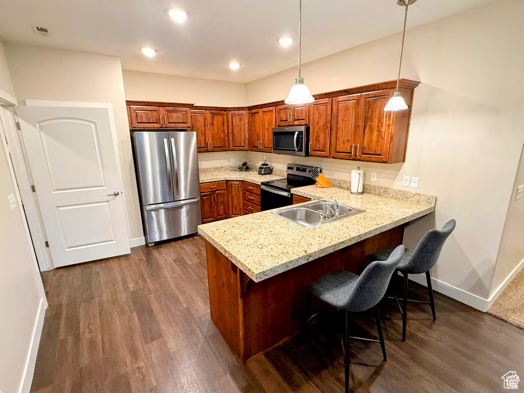 Kitchen with stainless steel appliances, a peninsula, brown cabinetry, dark wood finished floors, and a breakfast bar