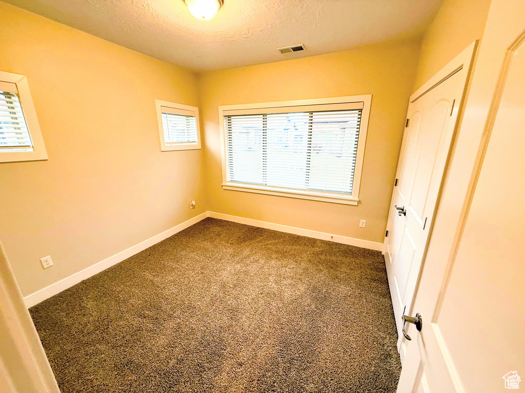Unfurnished bedroom featuring a textured ceiling and dark colored carpet