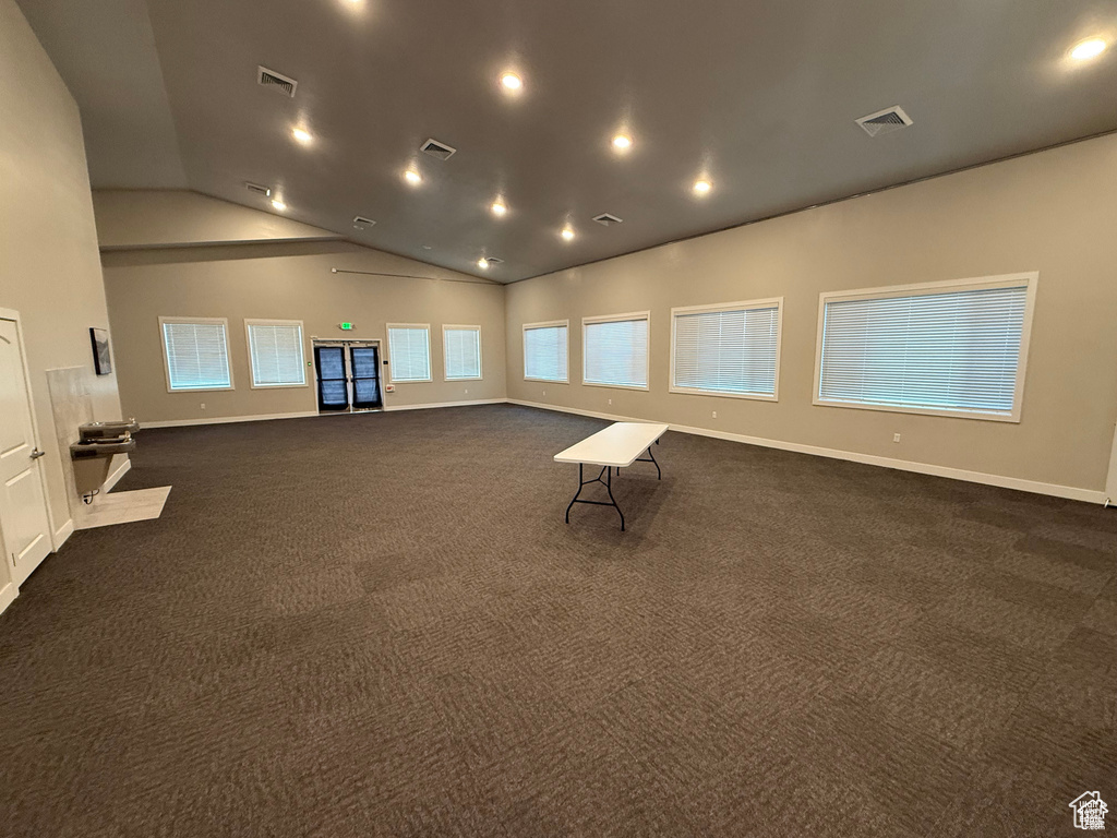 Empty room featuring healthy amount of natural light, lofted ceiling, dark colored carpet, and recessed lighting