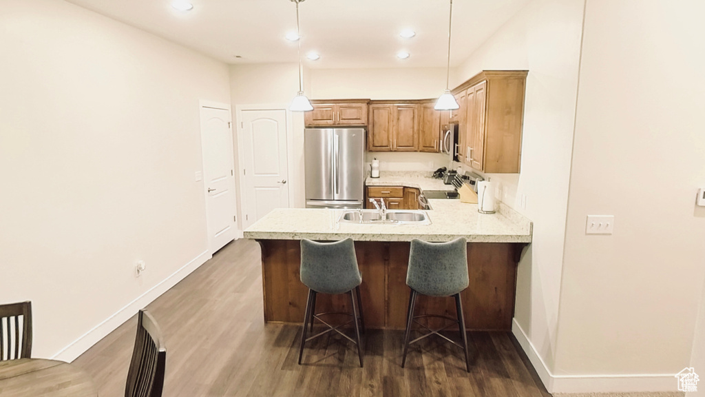 Kitchen featuring a peninsula, stainless steel appliances, a kitchen breakfast bar, dark wood-type flooring, and hanging light fixtures