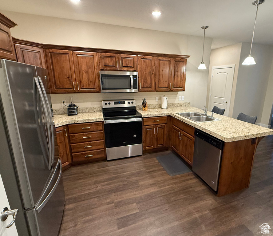 Kitchen with appliances with stainless steel finishes, a peninsula, dark wood finished floors, decorative light fixtures, and recessed lighting
