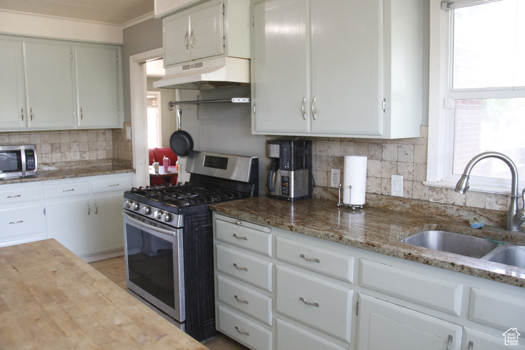Kitchen with stainless steel appliances, under cabinet range hood, backsplash, light stone counters, and white cabinets